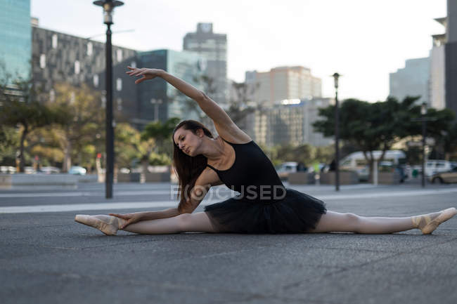 Bailarina de ballet femenina estirándose antes de bailar en la calle de la ciudad - foto de stock