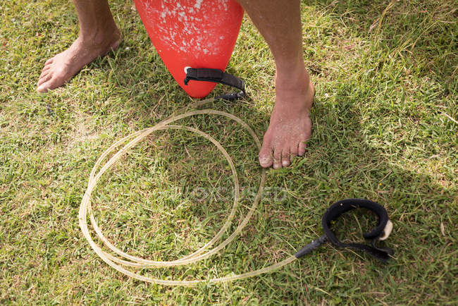 Low section of male surfer holding surfboard leash — Stock Photo