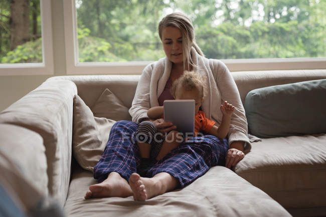 Mutter und Baby sitzen auf dem Sofa und nutzen zu Hause das digitale Tablet — Stockfoto