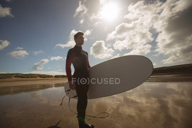 Surfista con tavola da surf che guarda il mare dalla spiaggia — Foto stock