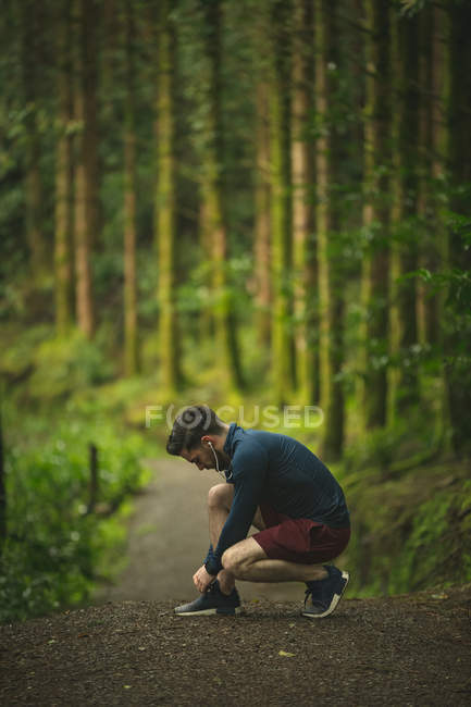 In forma uomo legando il suo lacci di scarpe nella foresta — Foto stock