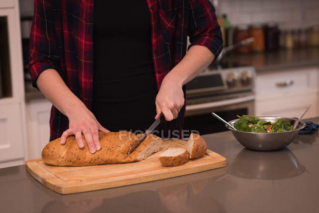 Woman cutting a loaf of bread in kitchen at home — Stock Photo