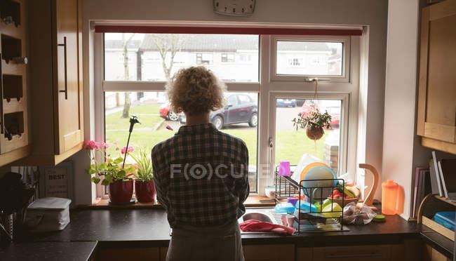Жінка дивиться крізь вікно на кухні вдома — стокове фото