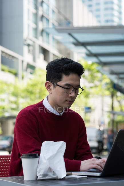 Hombre joven usando el ordenador portátil en la cafetería al aire libre - foto de stock