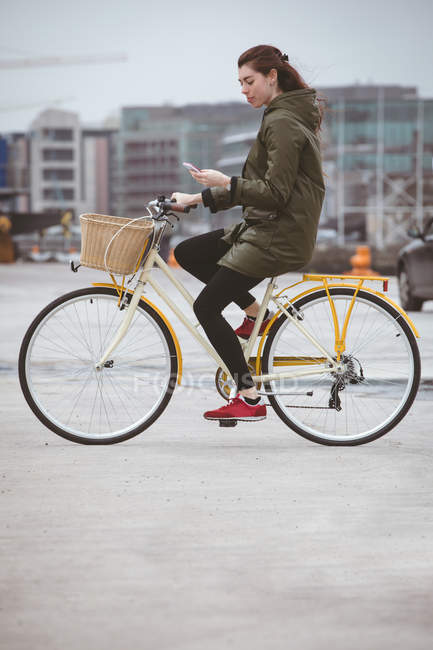 Belle femme utilisant un téléphone mobile tout en faisant du vélo sur la rue — Photo de stock