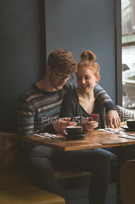 Молодая пара, использующая мобильные телефоны в кафе — стоковое фото