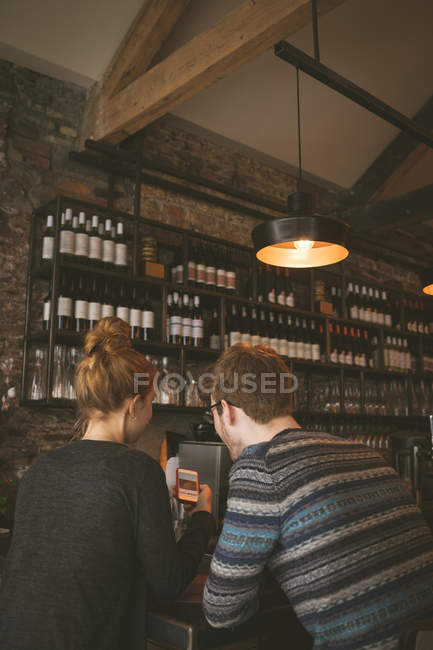 Rear view of couple looking at the mobile phone in the restaurant — Stock Photo