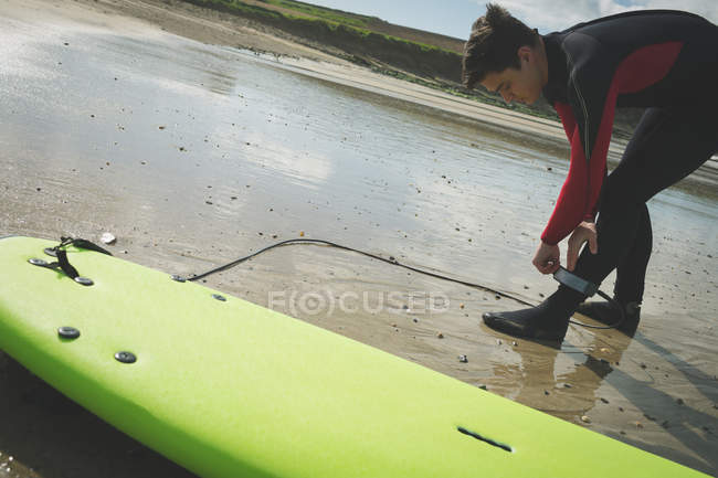 Surfeur attachant la corde de planche de surf à sa jambe sur la plage — Photo de stock
