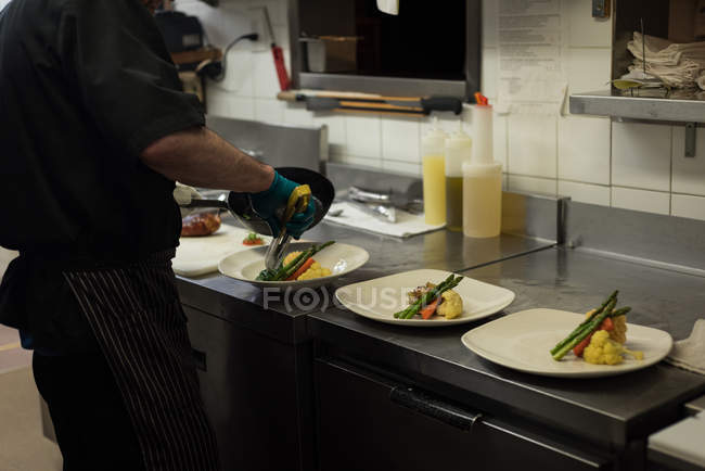 Sección media del chef masculino que sirve comida en un plato - foto de stock