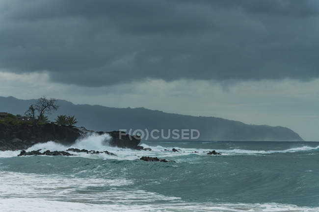 Olas de mar que se estrellan en la costa rocosa en el tiempo oscuro - foto de stock