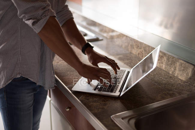 Sección media del hombre usando el ordenador portátil en la cocina en casa - foto de stock