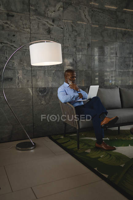 Продуманий бізнесмен сидить на дивані і використовує ноутбук — стокове фото