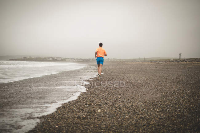Vista trasera del hombre corriendo en la orilla en la playa - foto de stock
