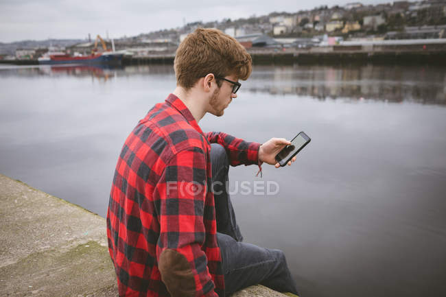Молодой человек использует свой мобильный телефон в порту — стоковое фото