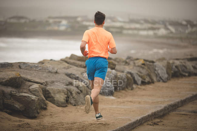 Vista trasera del hombre corriendo en el paseo marítimo en la playa - foto de stock
