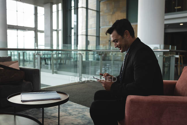 Улыбающийся бизнесмен с помощью мобильного телефона в офисе — стоковое фото