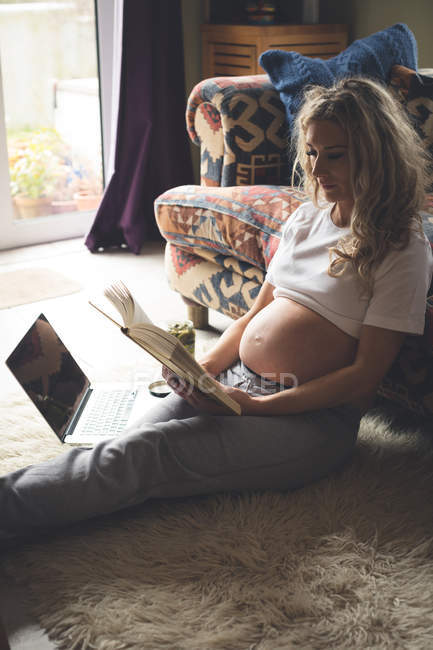 Donna incinta che legge un libro in soggiorno a casa — Foto stock