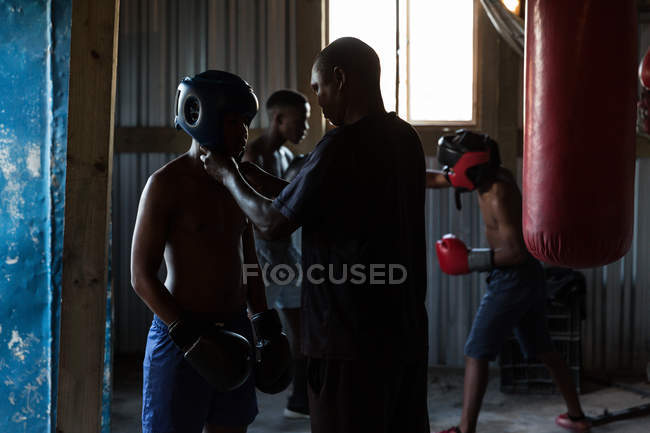 Trainer assisting male boxer to wear headgear in fitness studio — Stock Photo