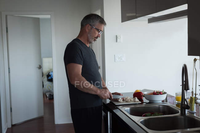 Homem cortando legumes na cozinha em casa — Fotografia de Stock