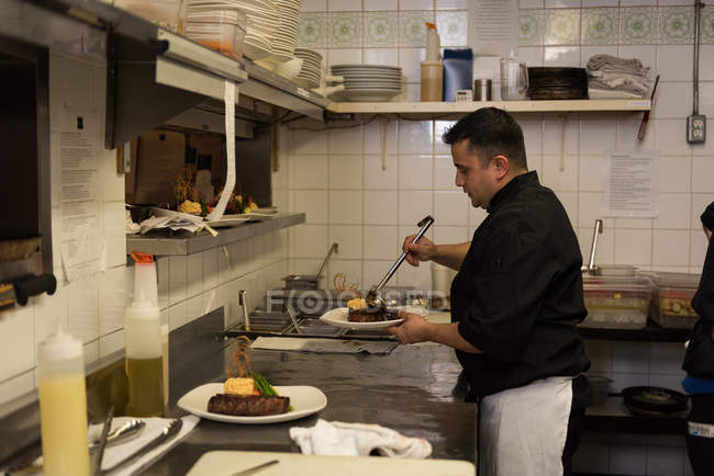 Chef masculino sirviendo comida en un plato en el restaurante - foto de stock
