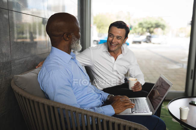 Dos hombres de negocios sonriendo mientras trabajan en el portátil - foto de stock