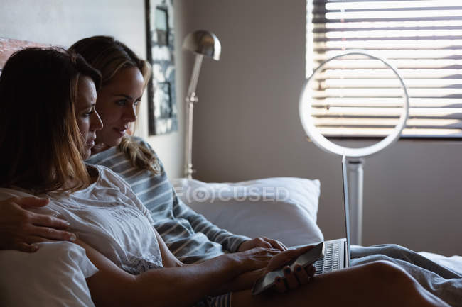 Casal de lésbicas usando laptop e telefone celular no quarto em casa — Fotografia de Stock