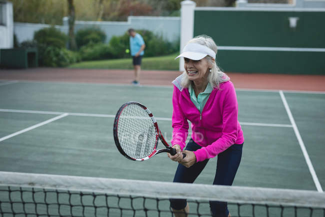 Счастливая старшая женщина играет в теннис на теннисном корте — стоковое фото