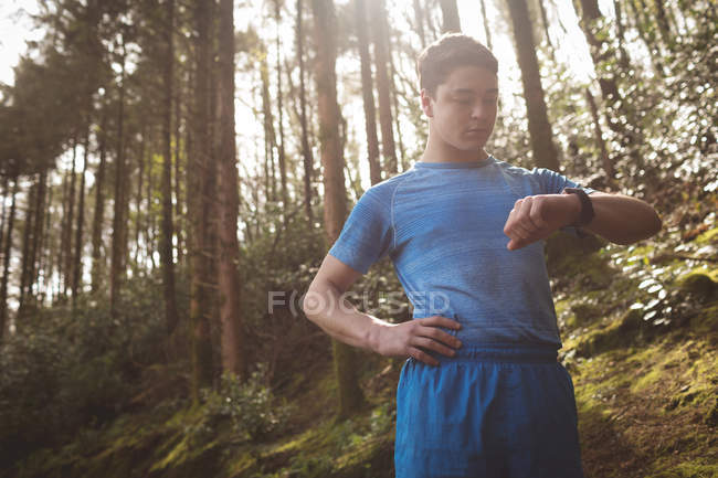 Молодой человек проверяет фитнес-часы в лесу — стоковое фото