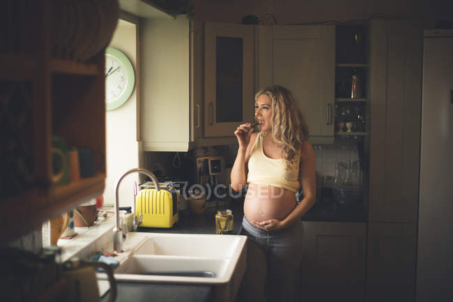 Embarazada mujer teniendo pepinillos en la cocina en casa - foto de stock