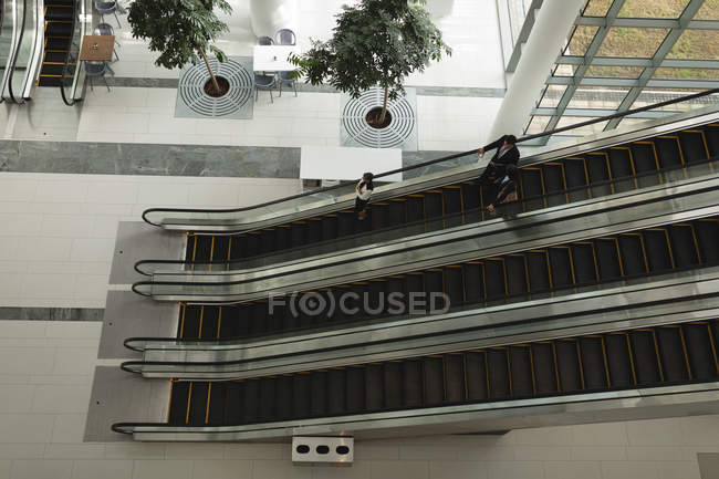 Деловые люди спускаются на эскалаторе в офисе — стоковое фото