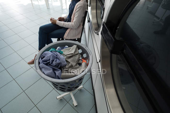 Visão de alto ângulo da mulher usando seu telefone enquanto espera na lavanderia — Fotografia de Stock