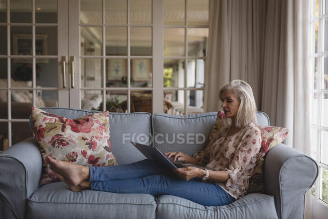 Senior woman using laptop on the sofa at home — Stock Photo
