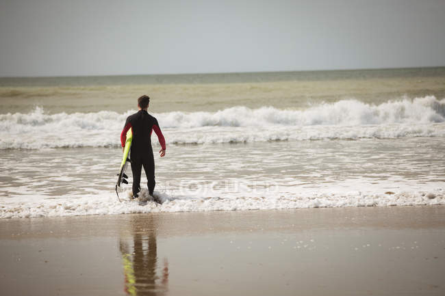 Rückansicht eines Surfers mit Surfbrett, der vom Strand aus auf das Meer blickt — Stockfoto