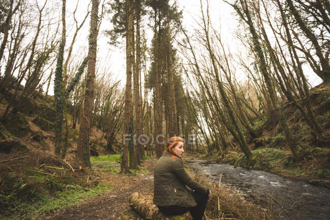 Jeune randonneuse assise au bord de la rivière dans la forêt — Photo de stock