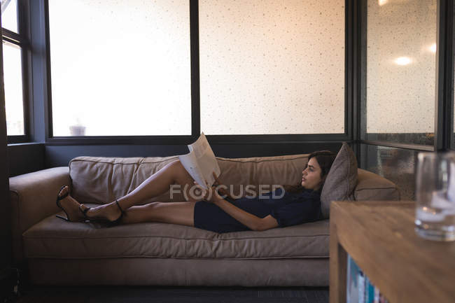 Geschäftsfrau liegt auf Sofa und liest Dokument im Büro — Stockfoto