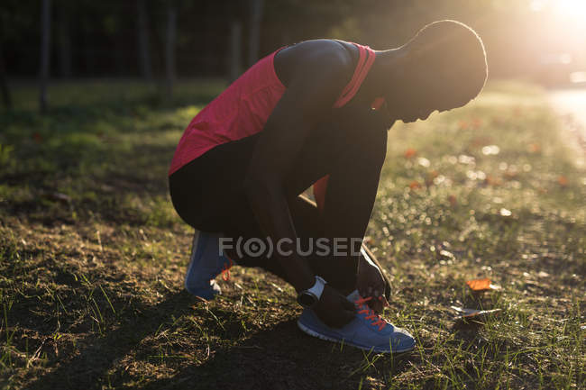 Female athlete tying her shoe lace in the forest — Stock Photo