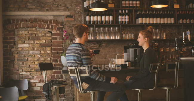 Pareja joven tomando café mientras está sentada en el mostrador del bar - foto de stock