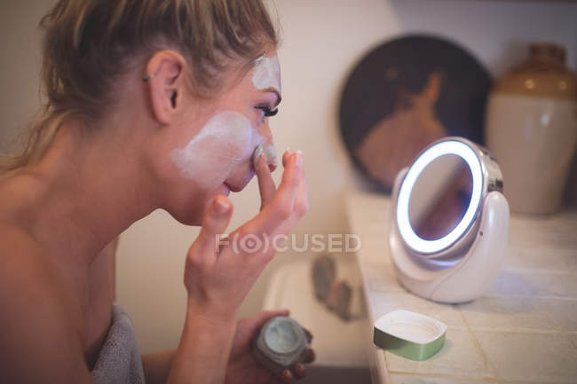 Femme appliquant la crème faciale dans la salle de bain à la maison — Photo de stock