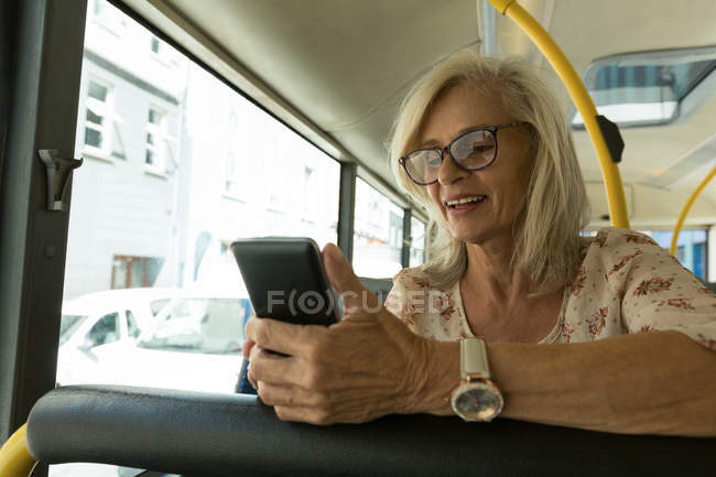 Seniorin benutzt Handy während Busfahrt — Stockfoto
