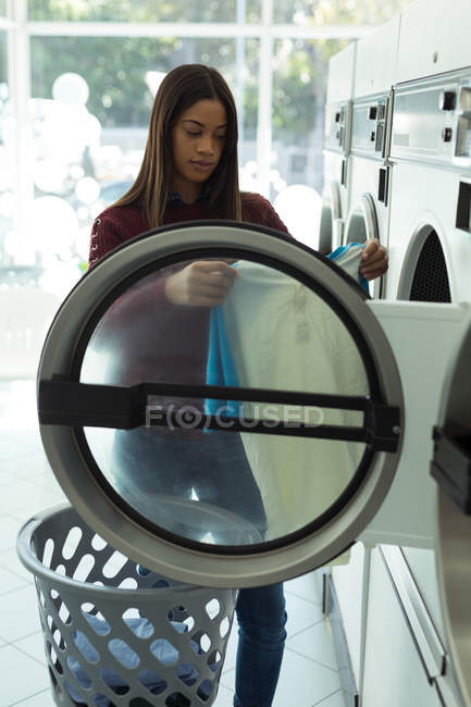 Jeune femme vérifiant ses vêtements dans la laverie automatique — Photo de stock
