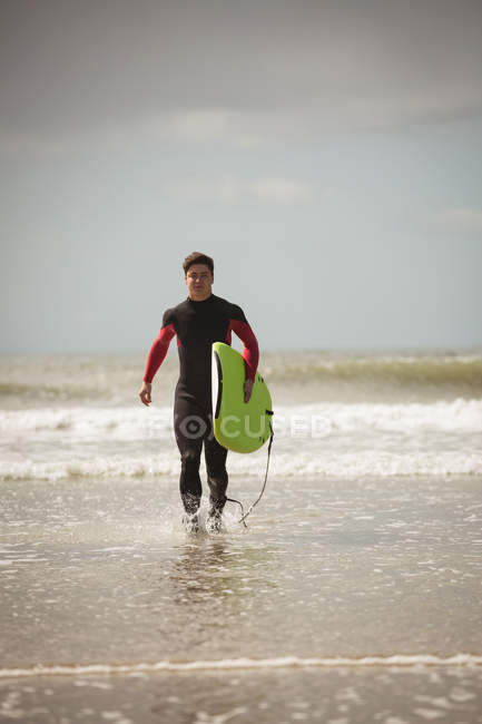 Determined surfer with surfboard running on the beach — Stock Photo