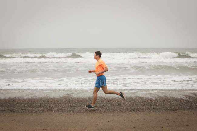Молодой человек бегает по берегу на пляже — стоковое фото