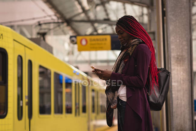 Mujer con estilo utilizando el teléfono móvil en la plataforma ferroviaria - foto de stock