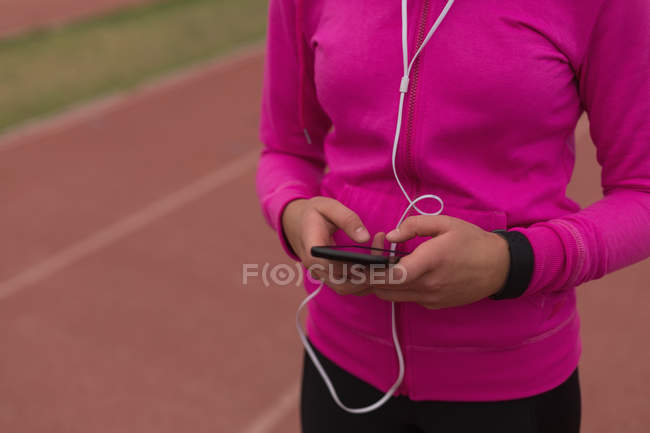 Sección media de la atleta femenina escuchando música en el teléfono móvil - foto de stock