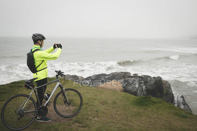 Молодой человек с велосипедом делает фото с мобильного телефона — стоковое фото
