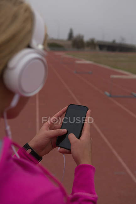 Female athlete listening music on mobile phone at running track — Stock Photo