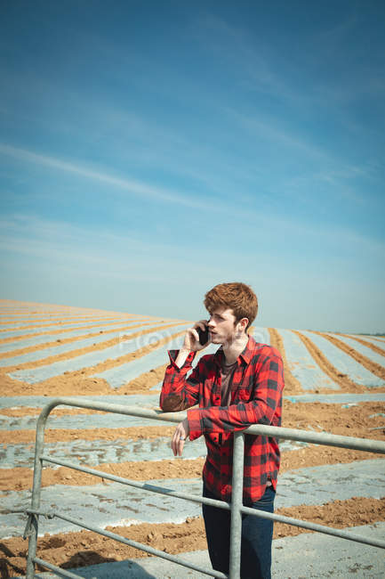 Чоловік спирається на перила і використовує мобільний телефон в полі в сонячний день — стокове фото