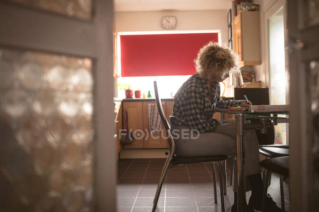 Giovane donna che scrive su un blocco note a casa — Foto stock