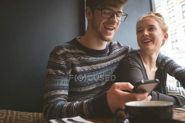 Happy couple using mobile phone in the cafe — Stock Photo