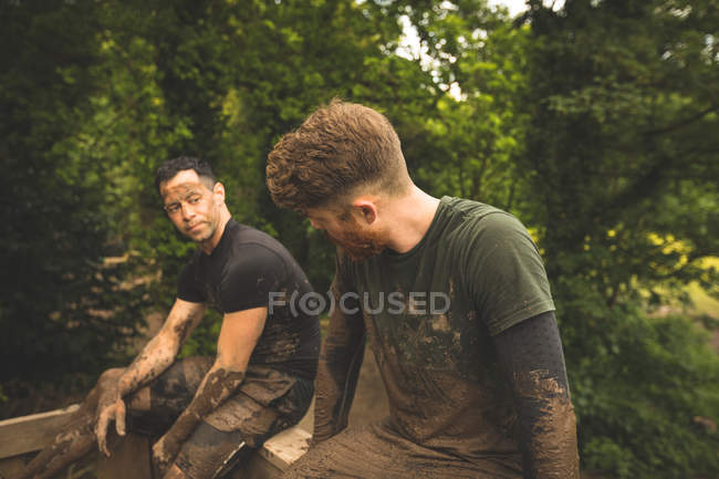 Ajuste los hombres que relajan sobre la carrera de obstáculos en el campo de entrenamiento - foto de stock